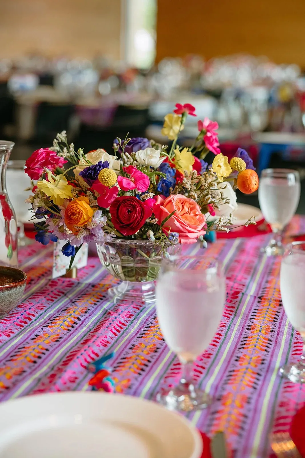 Colorful low centerpiece of roses, ranunculus and craspedia on a reception table